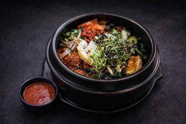 Bibimbap servi dans sa pierre noire, avec sauce rouge à côté