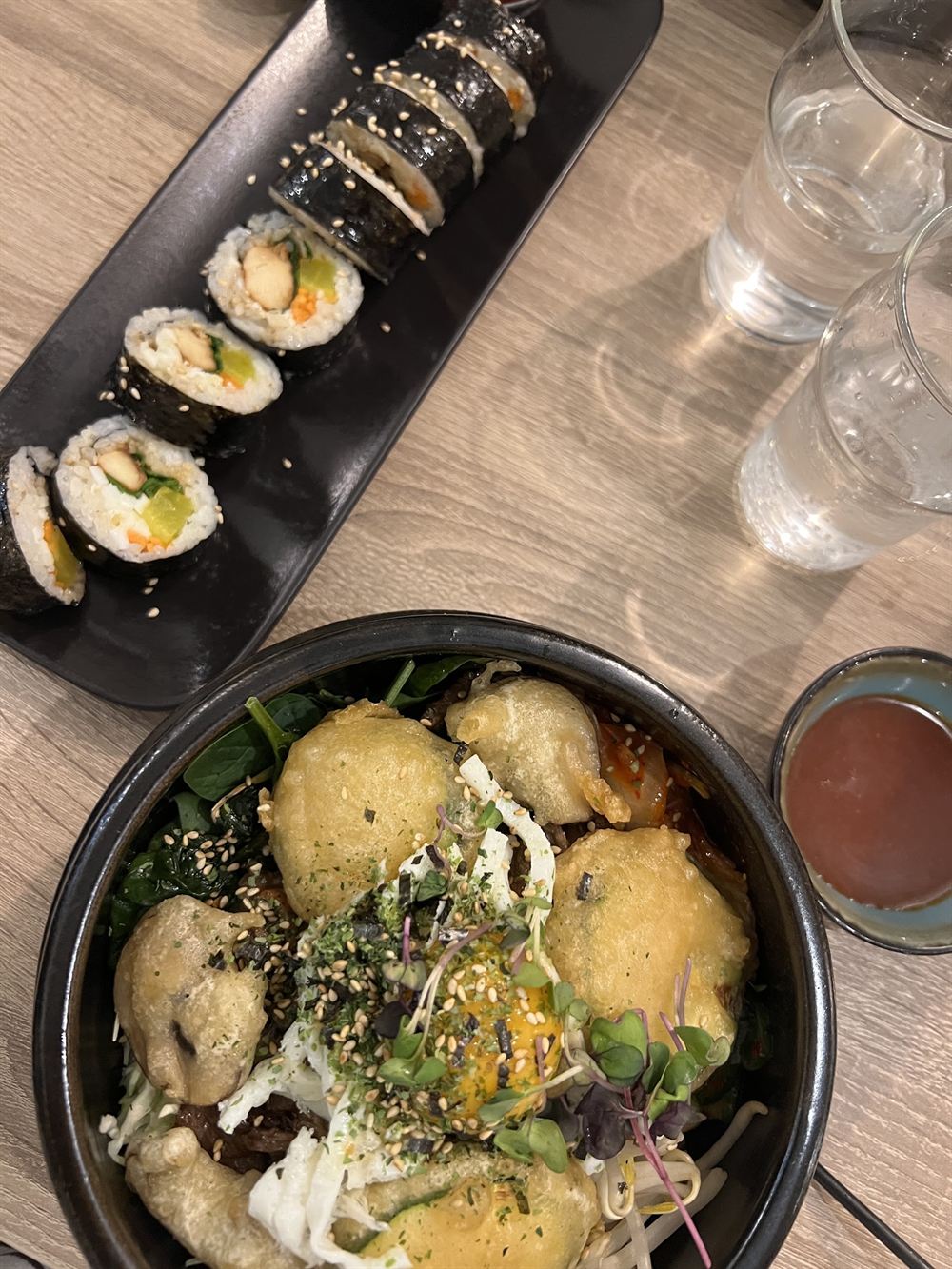 Kimbab coupés en rondelles sur une assiette noire, bibimbap au premier plan
