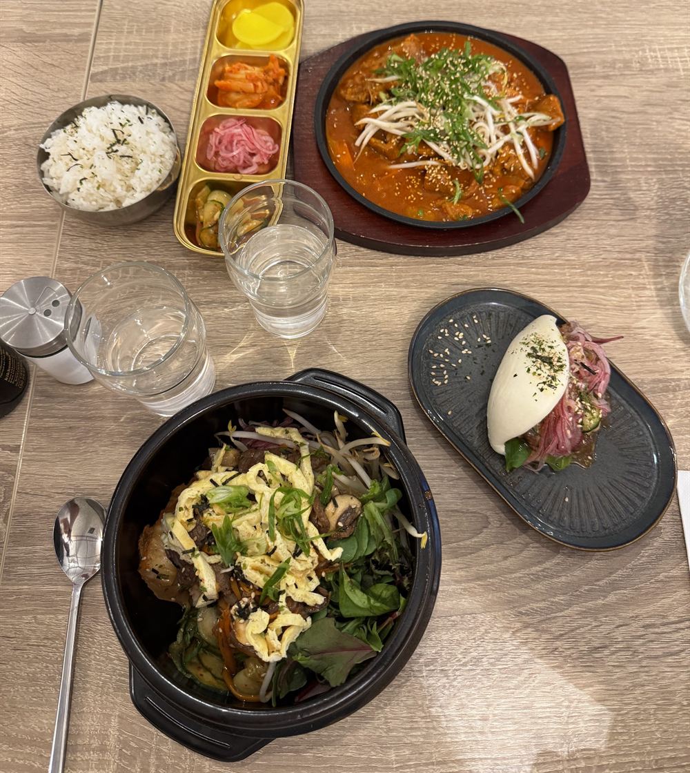 Table dressée : plat mijoté sur plaque chauffante, bibimbap, bau bun et assortiment de petits accompagnements